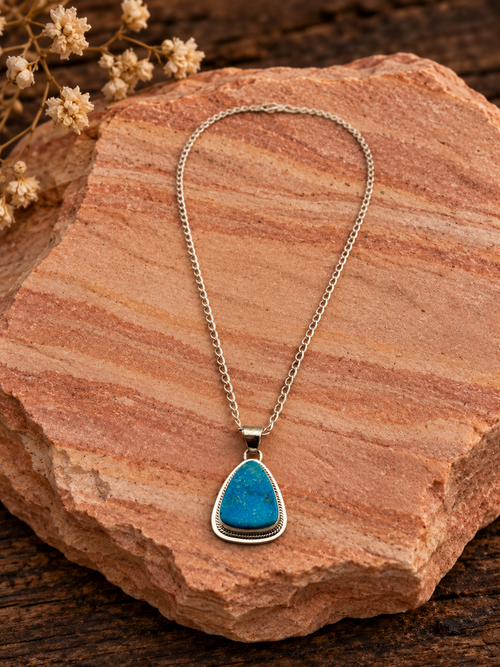Kingman turquoise rounded triangular pendant with included sterling silver chain on rose sandstone