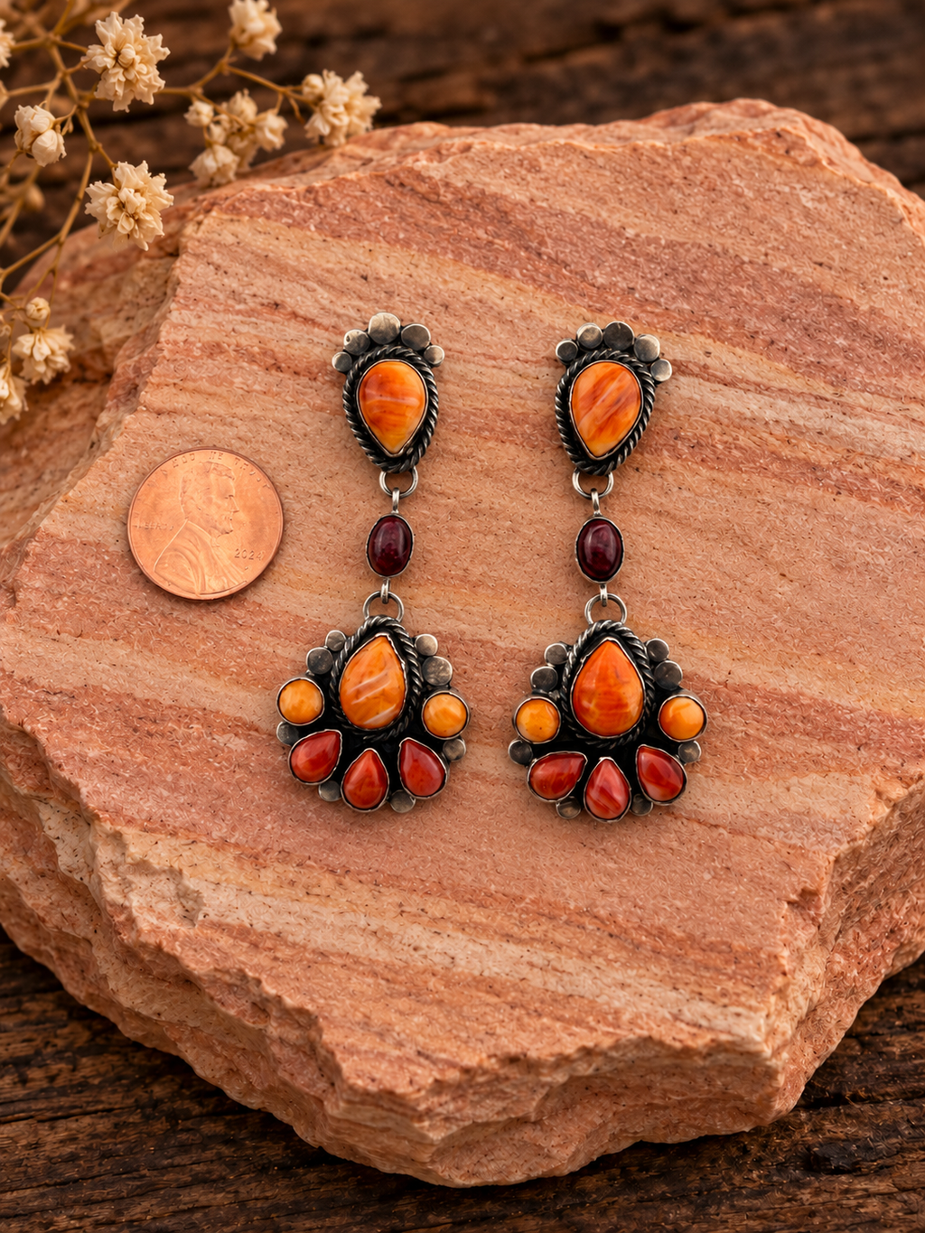 Orange and burgundy multistone dangle earrings beside a penny on rose sandstone