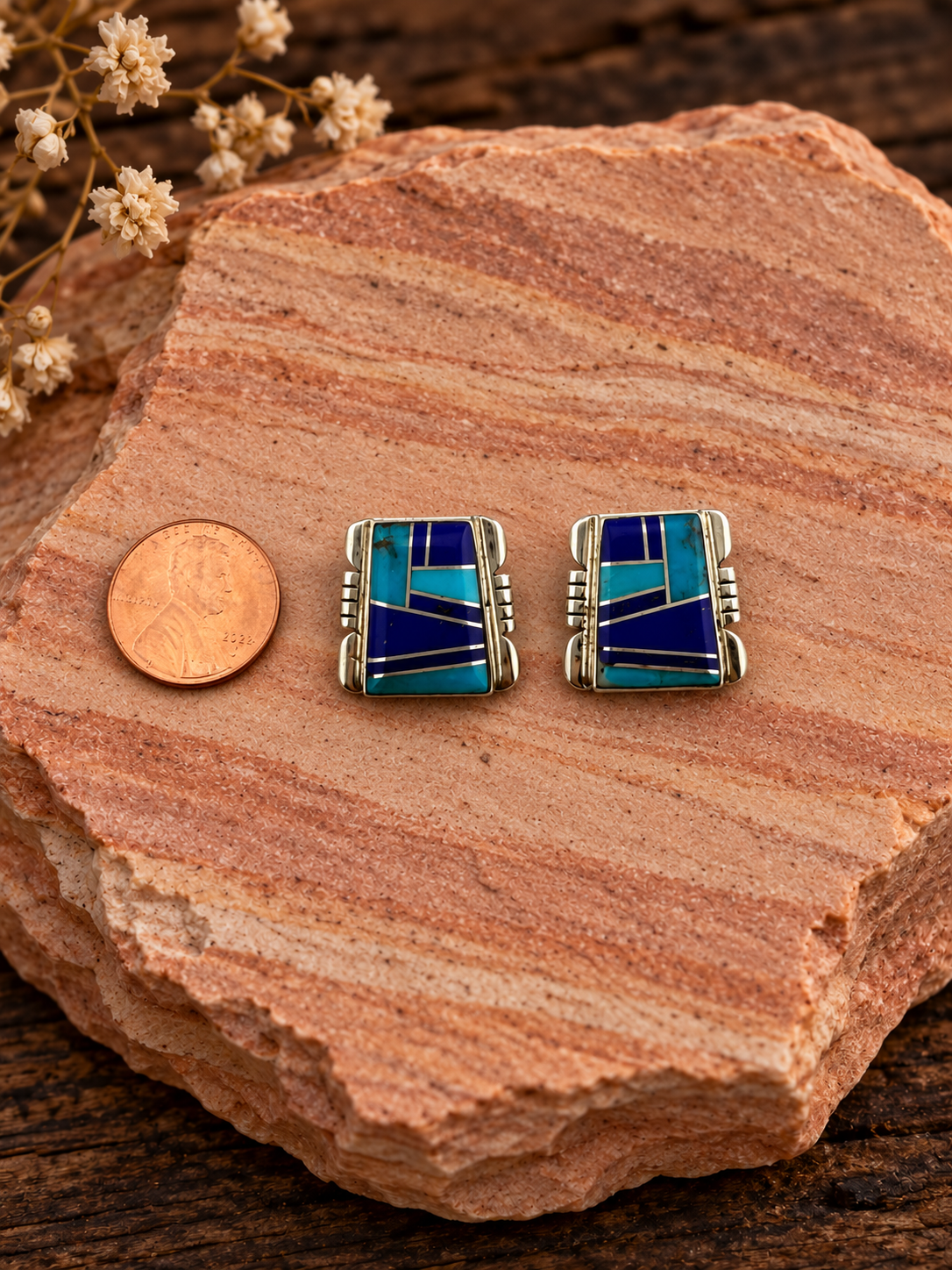 Blue geometric inlay rectangular earrings beside a penny on rose sandstone
