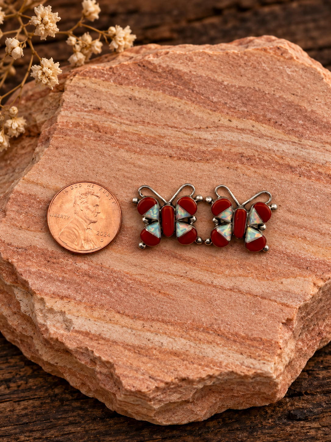 Red and iridescent butterfly earrings beside a penny on rose sandstone