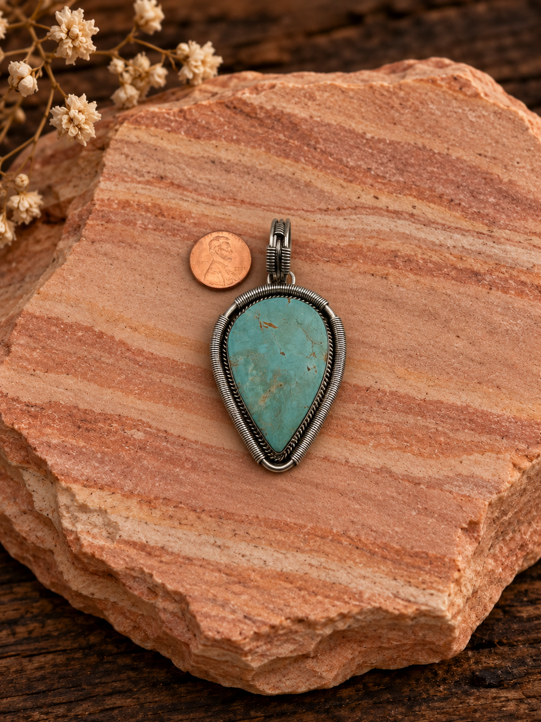 Turquoise teardrop sterling silver pendant with penny on rose sandstone background