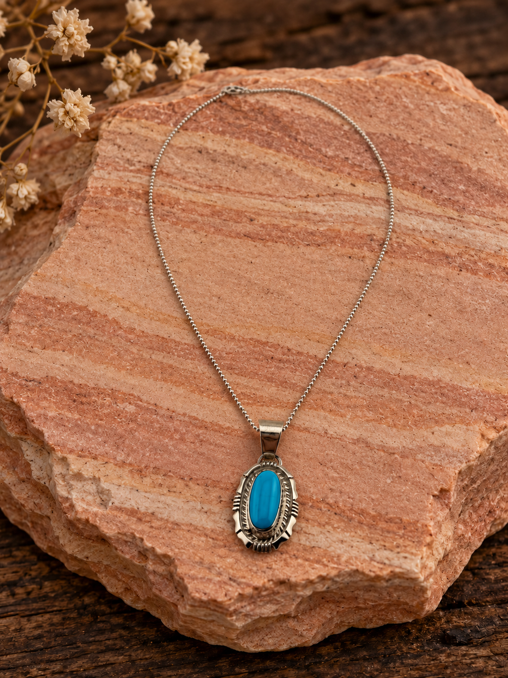 Oval turquoise pendant in ornate sterling silver setting with included sterling silver chain on rose sandstone